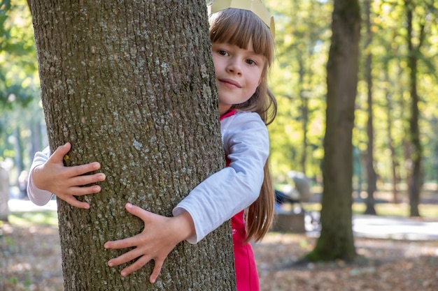 Ragazza del bambino che abbraccia un tronco di albero nel parco