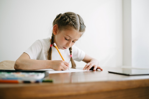 Ragazza del bambino che disegna e dipinge a casa mentre era seduto al tavolo