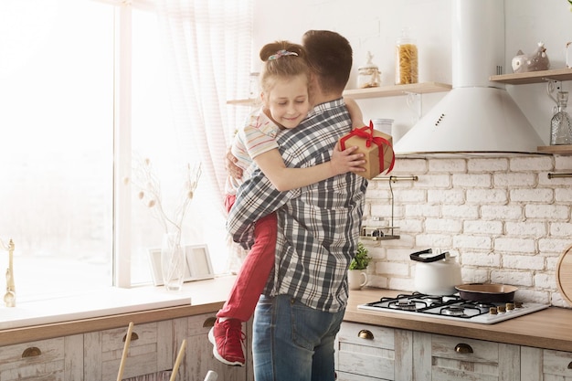 Ragazza del bambino che fa un regalo a suo padre nella cucina di casa. Felice famiglia amorevole e concetto di festa del papà.