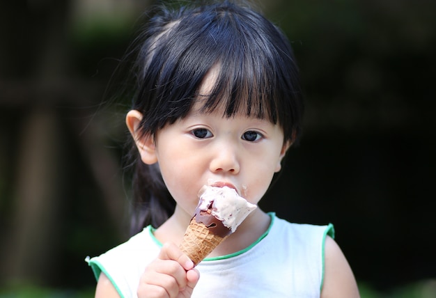 Ragazza del bambino che mangia il gelato nel giardino