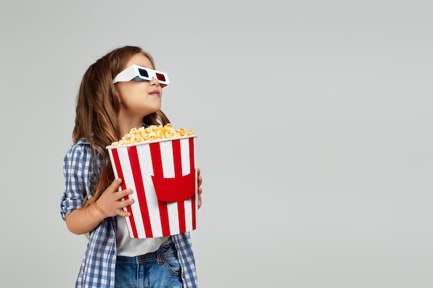 Ragazza del bambino che porta gli occhiali 3d redblue e che mangia popcorn