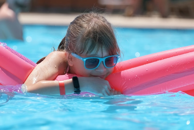 Ragazza del bambino che si rilassa sul sole estivo che nuota sul materasso gonfiabile in piscina durante le vacanze tropicali Concetto di attività estive