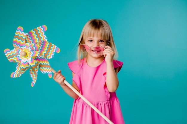 ragazza del bambino che sorride in occhiali da sole che tengono un mulino a vento su uno spazio blu