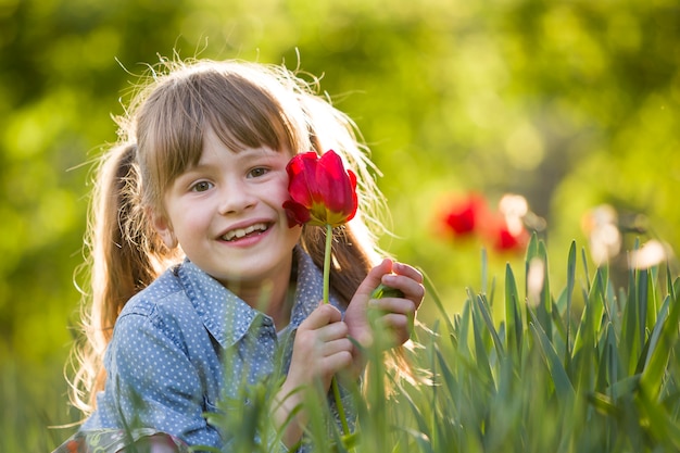 Ragazza del bambino con gli occhi grigi e capelli lunghi con fiore tulipano rosso brillante