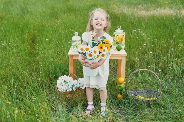 Ragazza del bambino con limonata. Limonata e fiori margherita sul tavolo. Mattina accogliente.