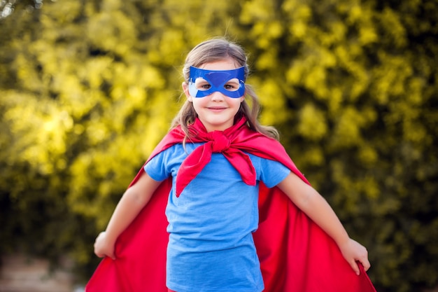 Ragazza del bambino del supereroe contro all'aperto verde