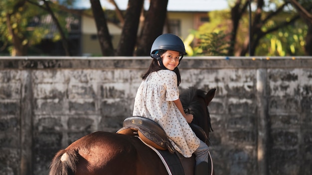 Ragazza del bambino della scuola asiatica con cavallo, equitazione o pratica di equitazione al ranch di cavalli.