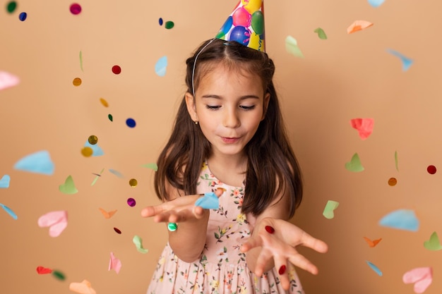 Ragazza del bambino di buon compleanno con i coriandoli su fondo beige