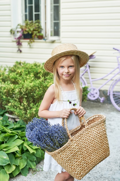 ragazza del bambino in cappello con un cestino di lavanda nel giardino in estate