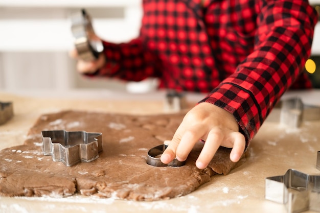 ragazza del bambino in pigiama rosso che cucina il pan di zenzero festivo nella cucina decorata di natale. biscotti di Natale