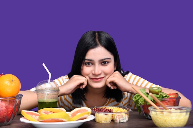 ragazza del buongustaio seduta al tavolo della frutta sorridendo con le mani sul tavolo guardando la modella pakistana indiana davanti