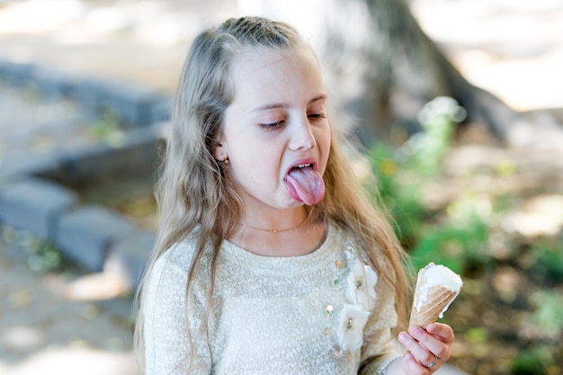 Ragazza del capretto con il cono gelato in mano Concetto di dolcetti d'estate Bambino della ragazza dei denti dolci con il gelato bianco nel cono della cialda Ragazza golosa sul viso disgustato mangia il gelato sfondo chiaro