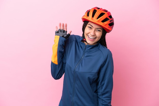 Ragazza del ciclista dell'adolescente isolata su fondo rosa che saluta con la mano con l'espressione felice