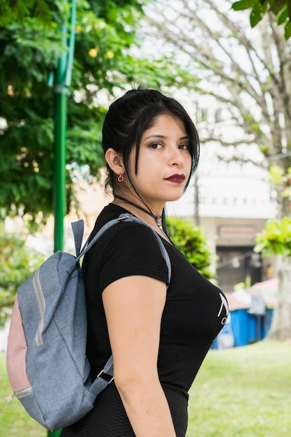 Ragazza del college latino con i capelli blu che cammina attraverso il parco vestita con una borsa nera e blu circondata