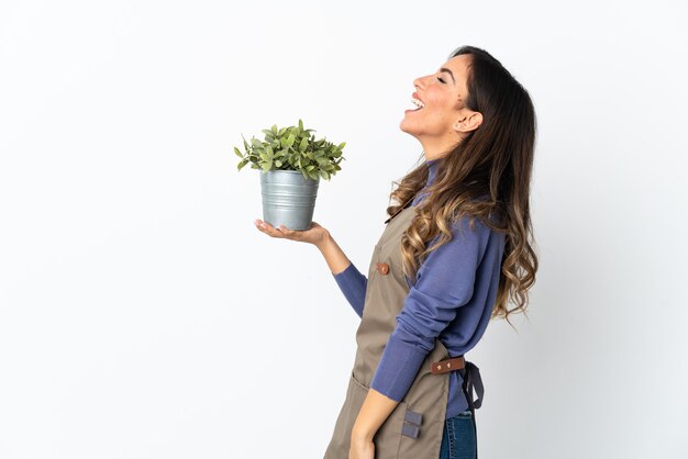 Ragazza del giardiniere che tiene una pianta isolata su priorità bassa bianca che ride in posizione laterale