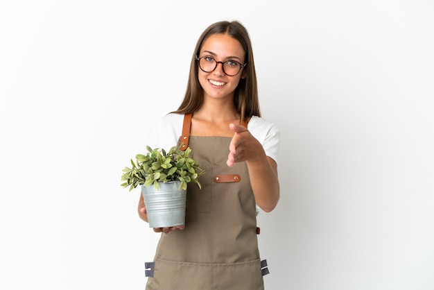 Ragazza del giardiniere che tiene una pianta sopra fondo bianco isolato che agita le mani per chiudere un buon affare