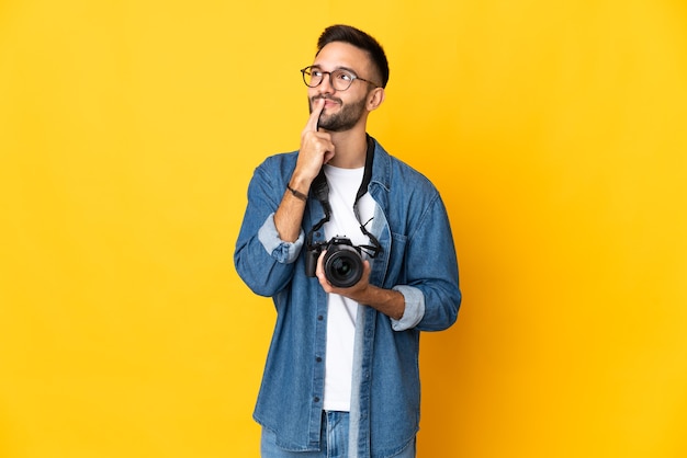 Ragazza del giovane fotografo isolata sulla parete gialla che ha dubbi mentre osserva in su