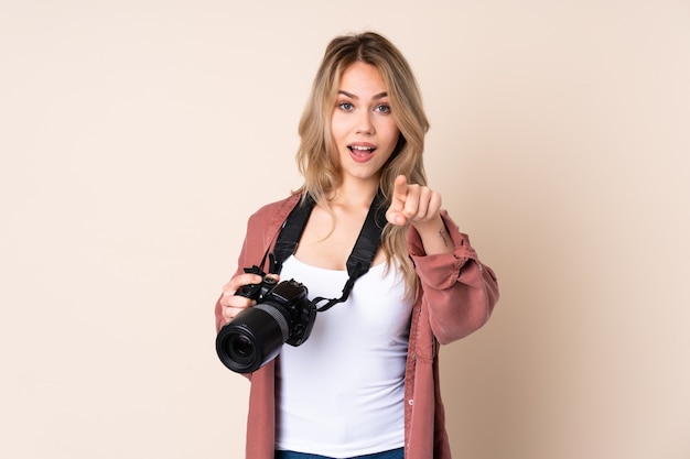 Ragazza del giovane fotografo sopra fondo isolato sorpreso e che punta davanti