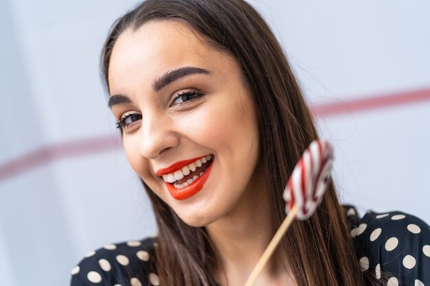 Ragazza del modello di moda con caramelle rotonde nelle mani. Bella giovane donna sorridente. Foto ritagliata.