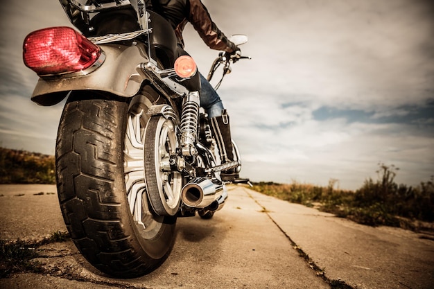 Ragazza del motociclista che guida su una moto. Vista dal basso delle gambe con stivali di pelle. Concentrati sulla ruota posteriore.