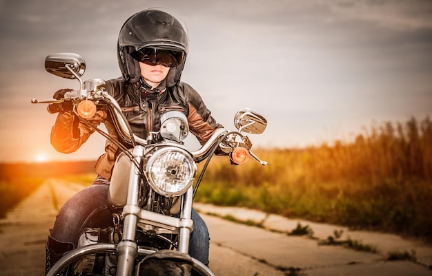 Ragazza del motociclista in una giacca di pelle e casco su una moto