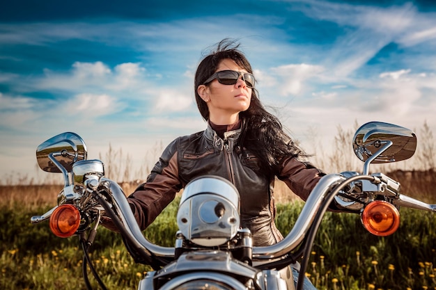 Ragazza del motociclista in una giacca di pelle e occhiali da sole che si siede sulla motocicletta