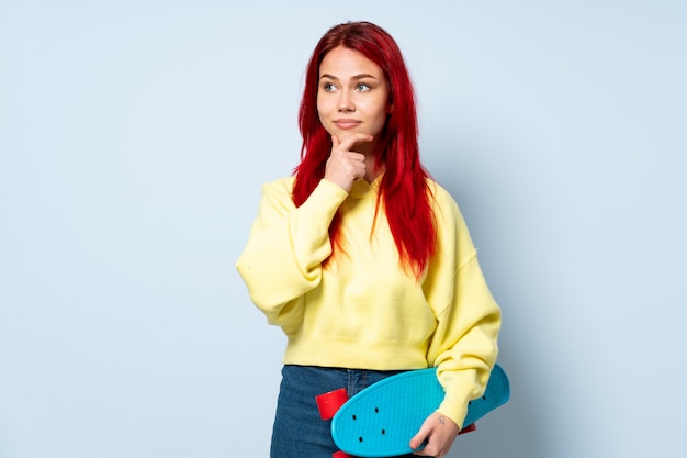 Ragazza del pattinatore dell'adolescente sulla parete bianca che pensa un'idea mentre guardando su