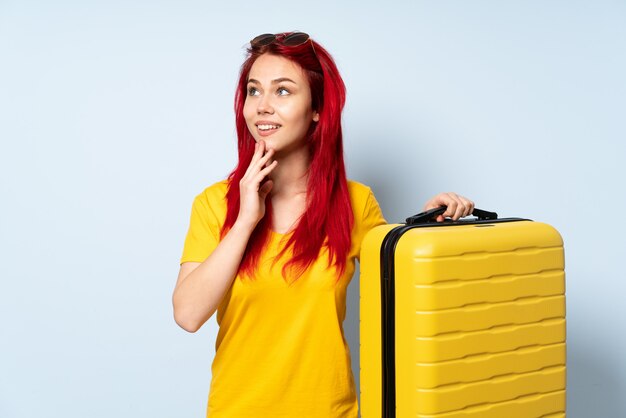 Ragazza del viaggiatore che giudica una valigia isolata sul cercare blu mentre sorridendo