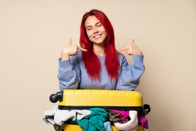 Ragazza del viaggiatore con una valigia piena di vestiti isolati su beige fiero e soddisfatto di sé