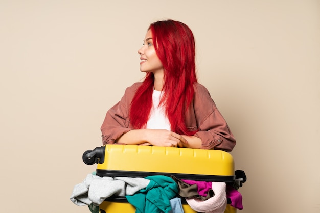 Ragazza del viaggiatore con una valigia piena di vestiti isolati sul fondo beige che sembra laterale