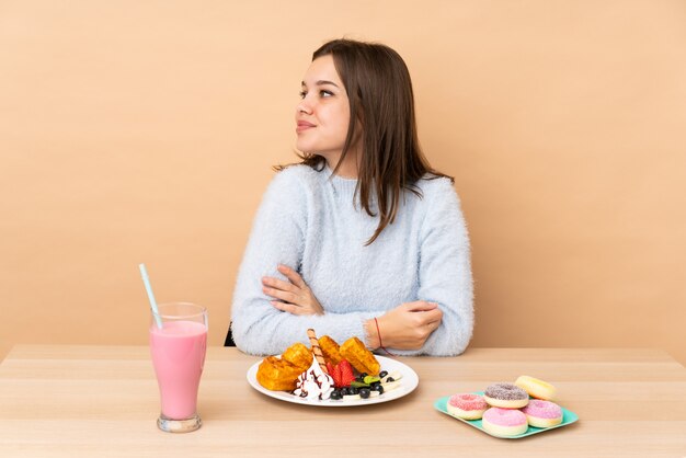 Ragazza dell'adolescente che mangia le cialde su risata beige nella posizione laterale