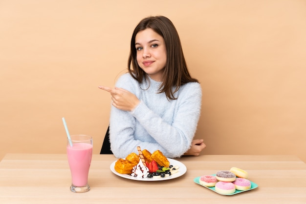 Ragazza dell'adolescente che mangia le cialde sul beige che indica il lato per presentare un prodotto