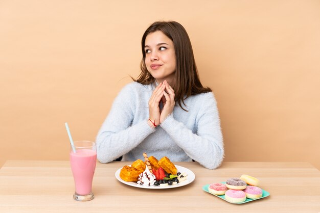 Ragazza dell'adolescente che mangia le cialde sul beige che traccia qualcosa