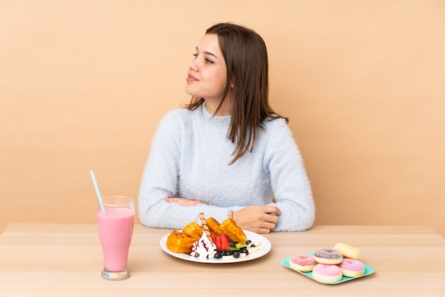 Ragazza dell'adolescente che mangia le cialde sulla parete beige nella posizione laterale