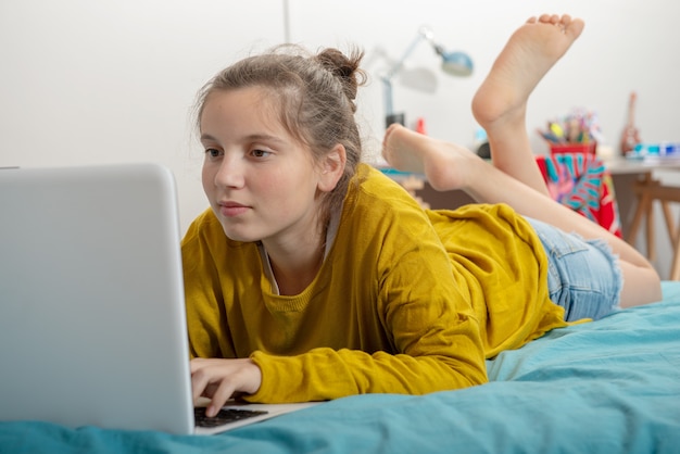 Ragazza dell&#39;adolescente che si trova sul letto, facendo uso del computer portatile