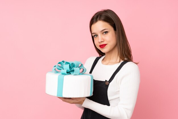 Ragazza dell'adolescente che tiene un grande dolce sulla parete rosa