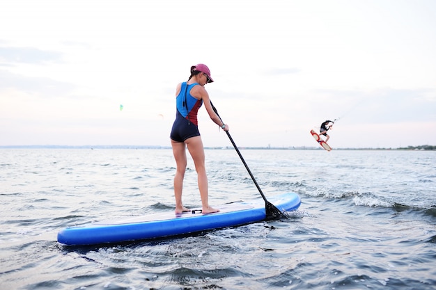 Ragazza dell'adolescente con il bordo del SUP sul mare. Attività di paddle surf