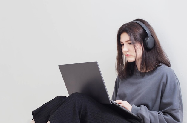 Ragazza dell'adolescente con il computer portatile che si siede sul pavimento nella stanza bianca