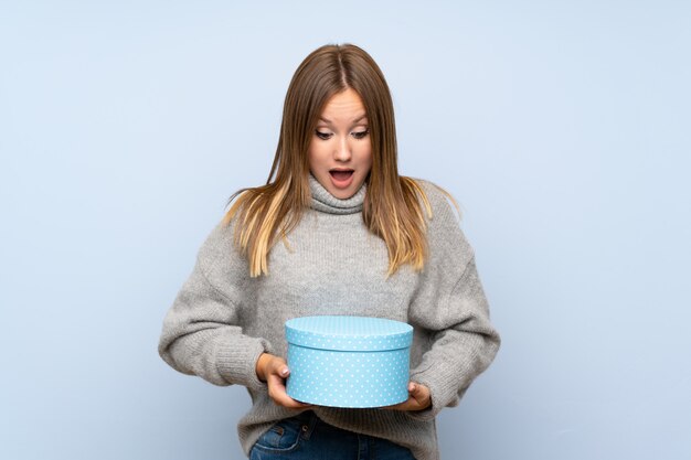 Ragazza dell'adolescente con il maglione sopra il contenitore di regalo blu isolato della tenuta del fondo