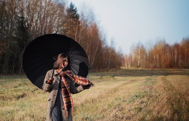 Ragazza dell'adolescente con l'ombrello nero nel campo di autunno