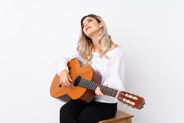 Ragazza dell'adolescente con la chitarra sopra bianco isolato che osserva in su mentre sorridendo