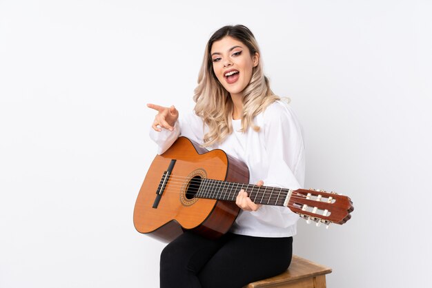 Ragazza dell'adolescente con la chitarra sopra bianco isolato sorpreso e puntando il dito verso il lato