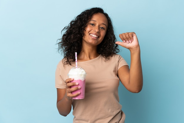 Ragazza dell'adolescente con milkshake alla fragola isolato su blu orgoglioso e soddisfatto di sé