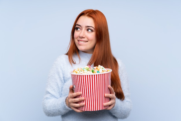 Ragazza dell'adolescente della testarossa sopra l'azzurro che tiene un grande secchio di popcorn