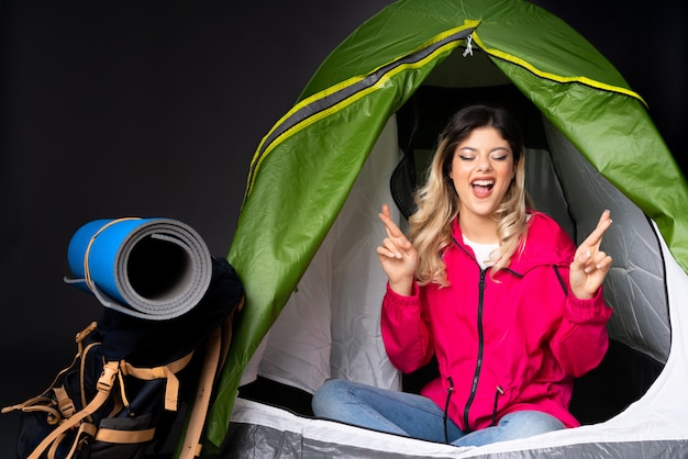 Ragazza dell'adolescente dentro una tenda verde di campeggio sulla parete nera con l'incrocio delle dita