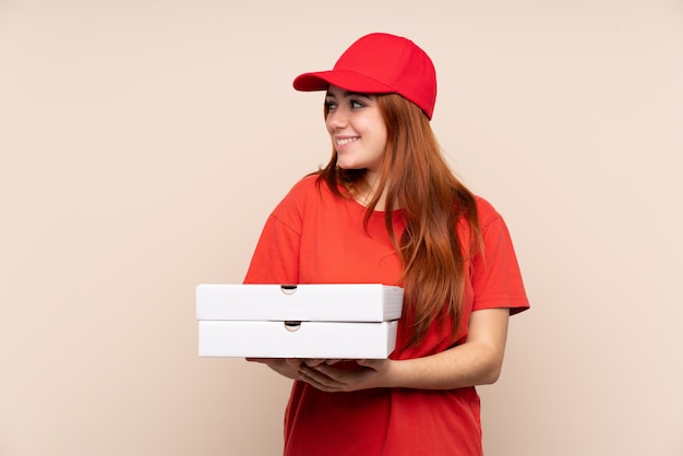 Ragazza dell'adolescente di consegna della pizza che tiene una pizza sopra la parete isolata che guarda al lato