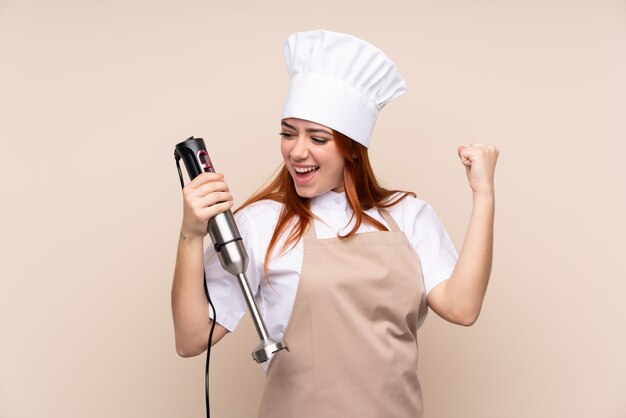 Ragazza dell'adolescente di Redhead che usando il miscelatore della mano sopra che celebra una vittoria