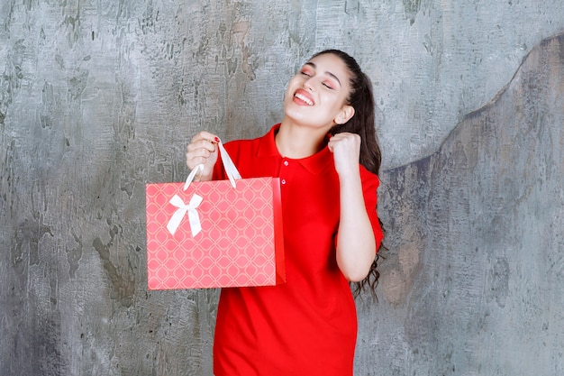 Ragazza dell'adolescente in camicia rossa che tiene un sacchetto della spesa rosso.