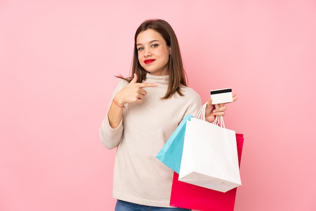 Ragazza dell'adolescente isolata sui sacchetti della spesa rosa della tenuta della parete e una carta di credito