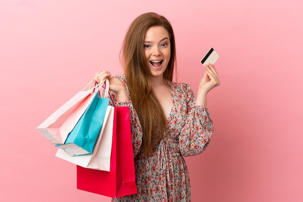 Ragazza dell'adolescente sopra fondo rosa isolato che tiene le borse della spesa e sorpresa